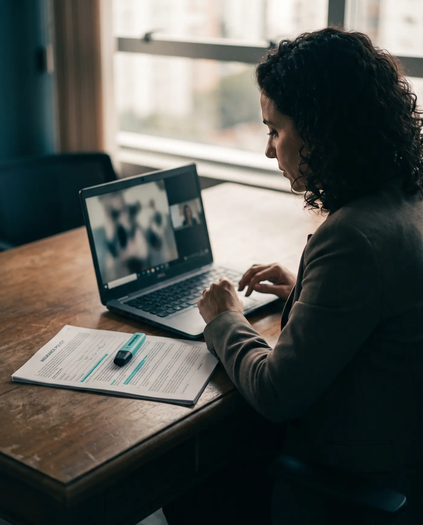 Corretora numa videochamada, com a apólice impressa e marcada ao lado do notebook